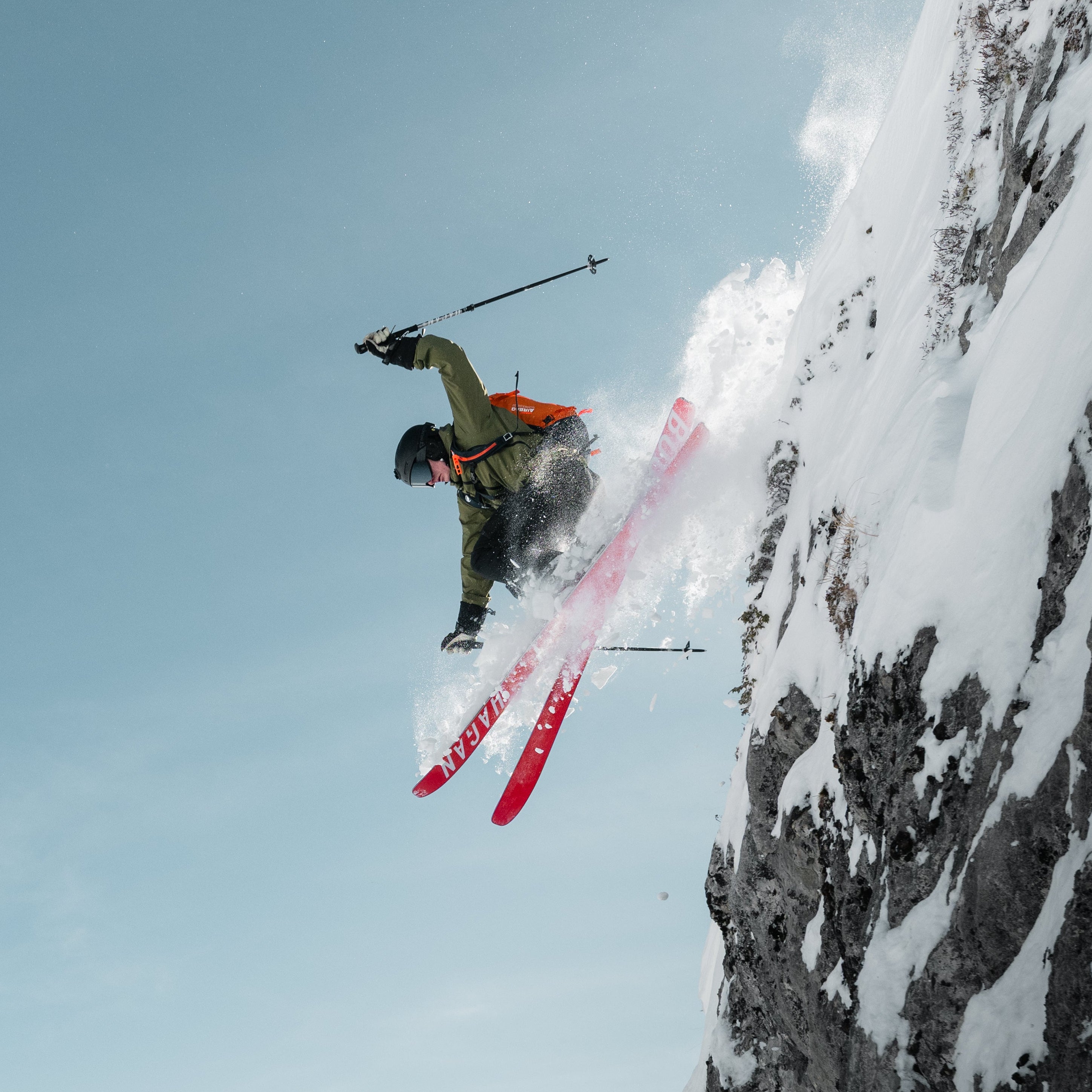 Skier performing a jump off a snowy cliff with mountains in the background